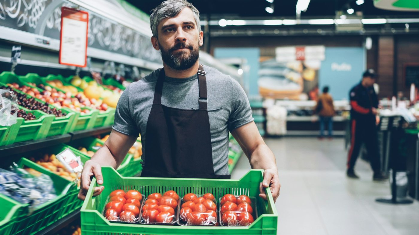 A grocer holding a crate of fresh tomatoes
